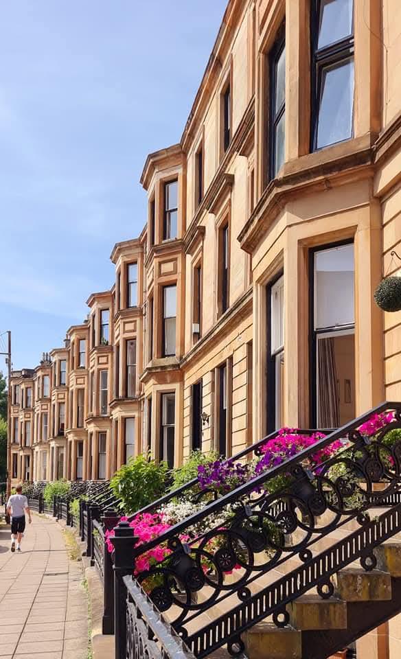 A sunny Glasgow street lined with traditional sandstone tenements and flower-filled steps